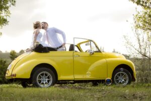 A wedding photo of a couple kissing while sitting in a yellow Volkswagen beetle convertible