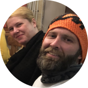 Headshot of a couple, Craig wearing an orange hat and beard, and Roz a smiling blonde woman beside him